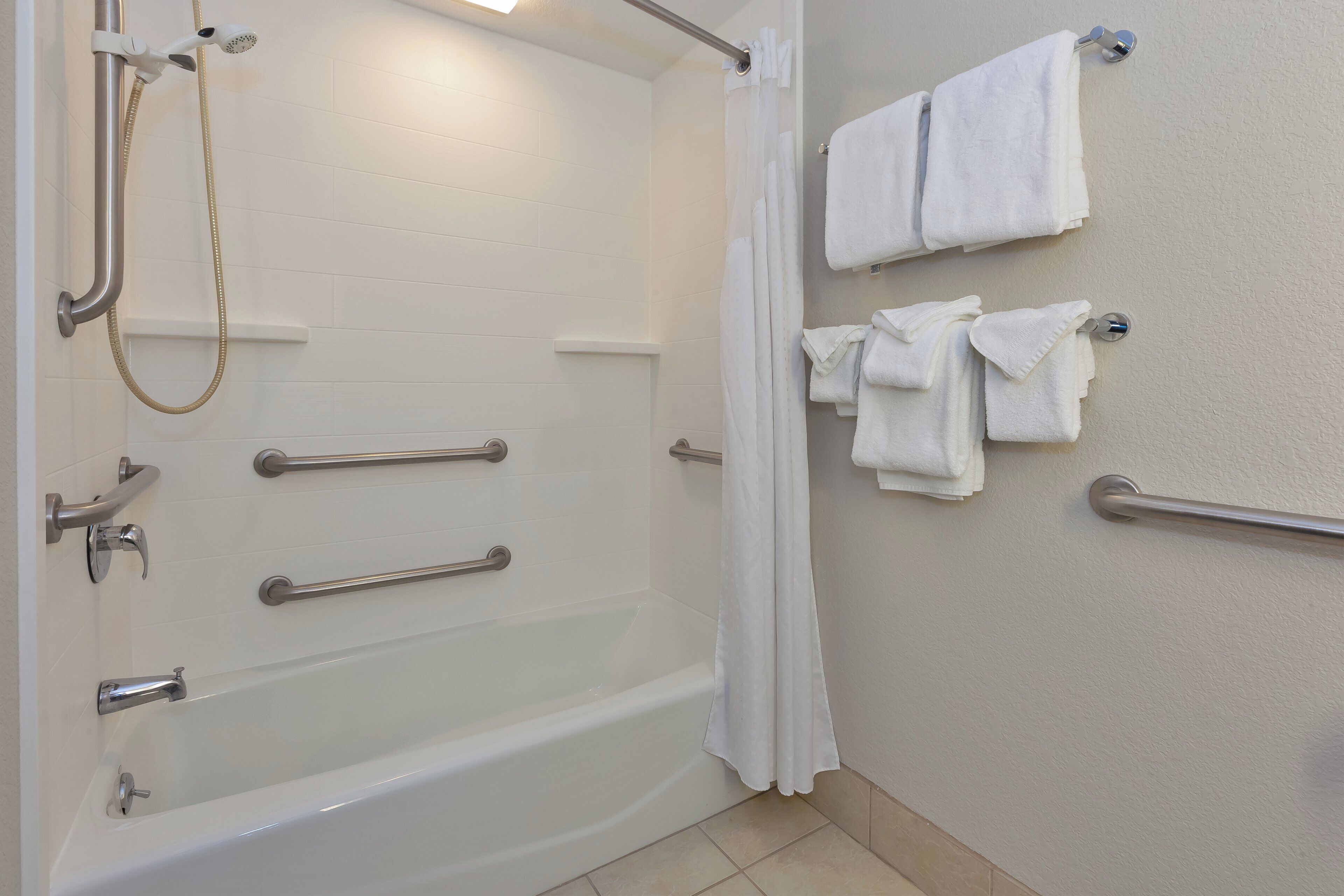 Un baño con bañera, ducha y barras de apoyo.