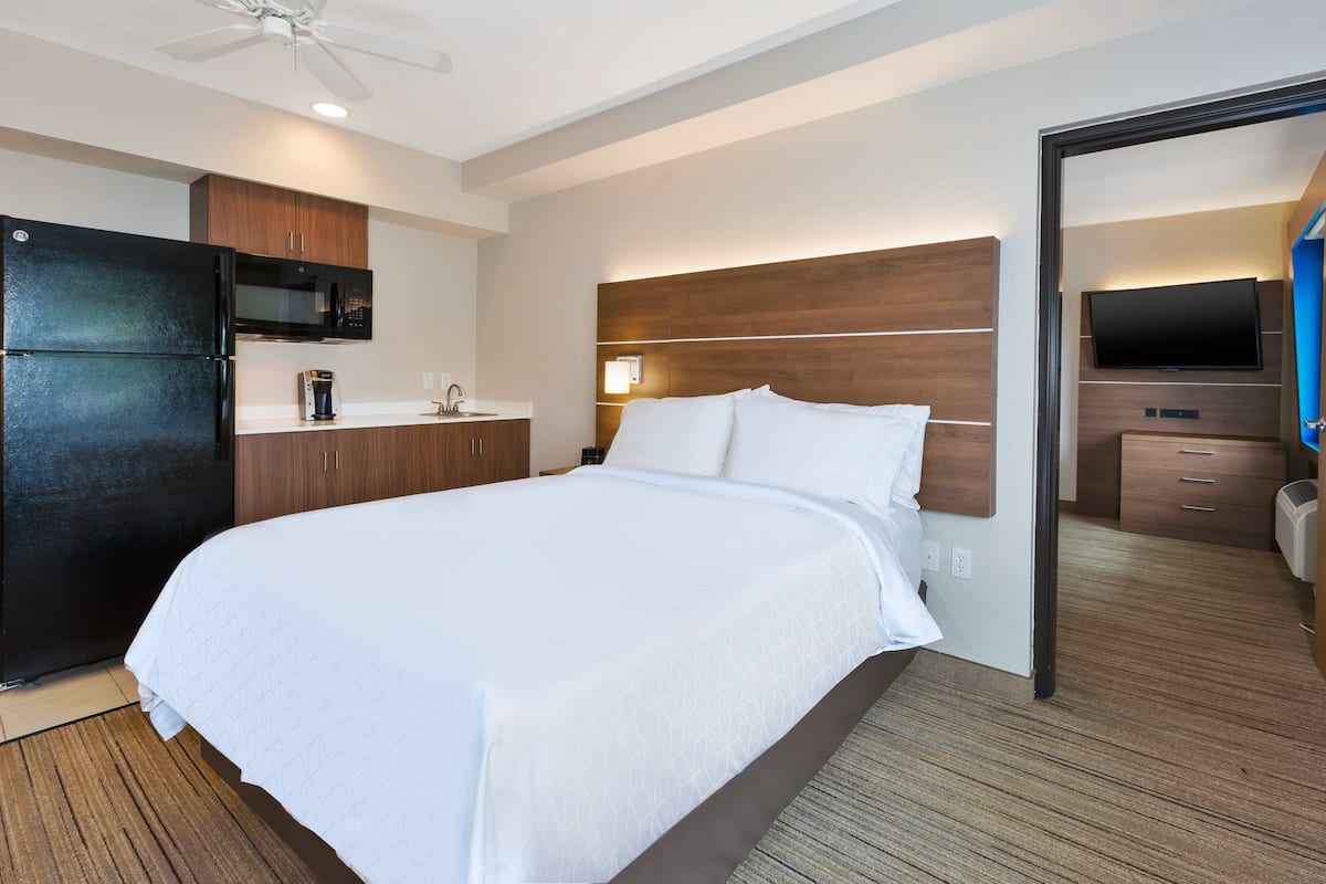 Una habitación de hotel con una cama grande, televisión integrada, microondas y una pequeña kitchenette.