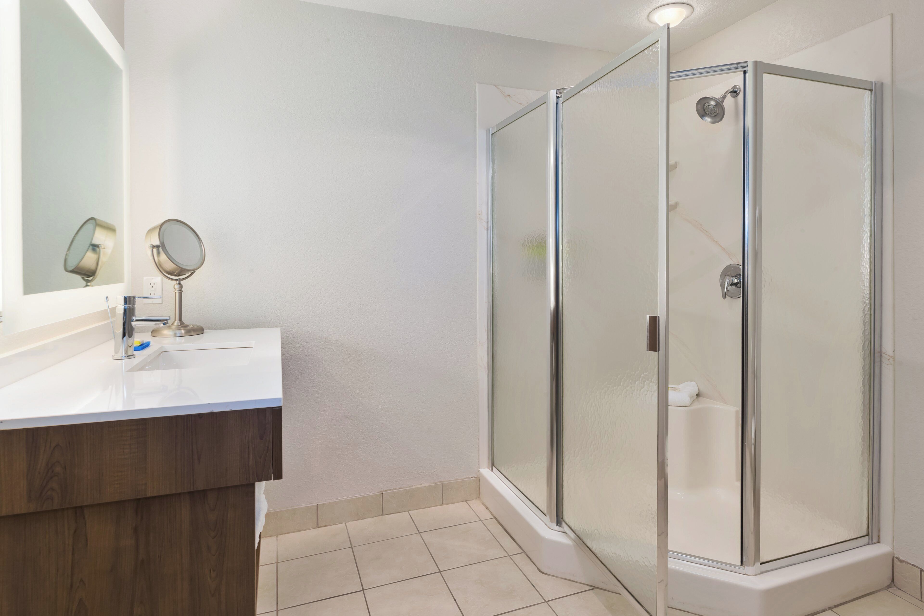 A bathroom with a glass-enclosed shower, a wooden vanity, and a mirror with two round mirrors.