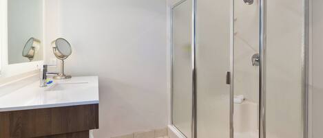 Un baño con ducha de vidrio, tocador de madera y espejo con dos espejos redondos.