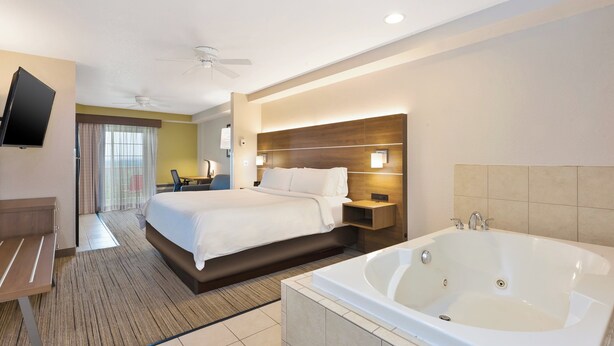 A hotel room with a large bed, a sitting area, a bathroom with a bathtub, and a television mounted on the wall. - Holiday Inn Express & Suites Petoskey by IHG (Petoskey)
