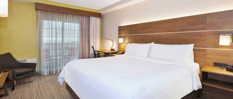 Habitación de hotel con una cama grande, un escritorio, una silla y un ventanal con cortinas.