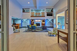 A spacious lobby with a high ceiling, a fireplace, and a seating area with chairs and a sofa.