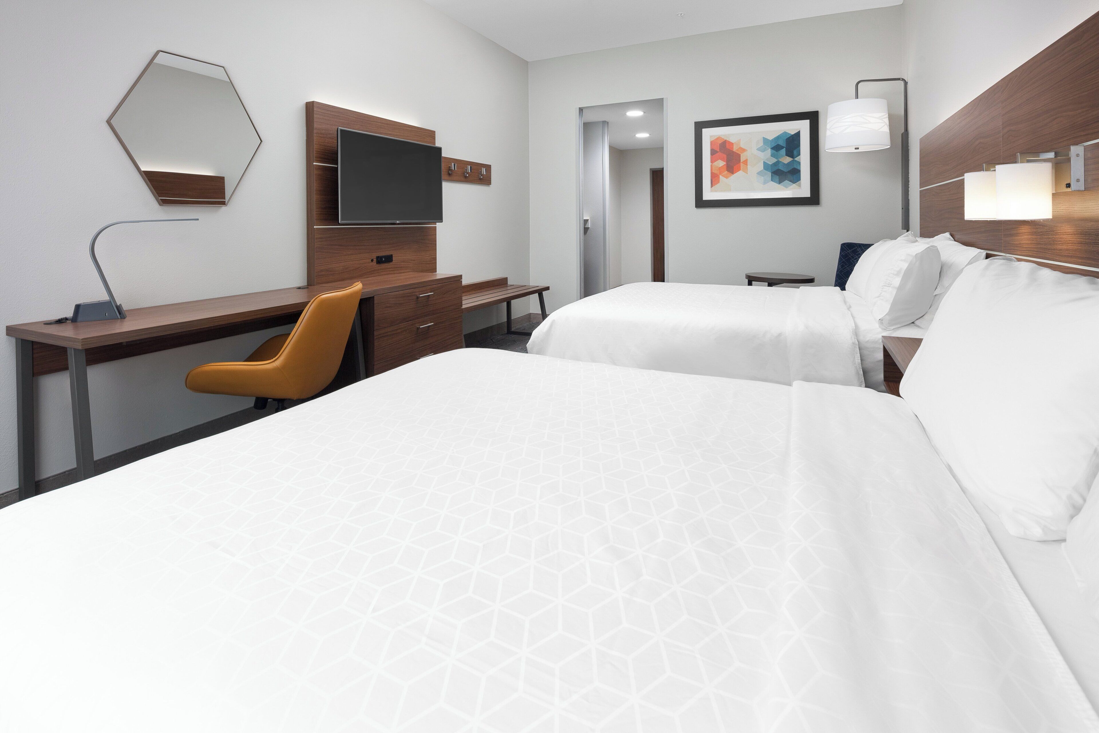 A hotel room with a bed, a desk, a chair, a television, and a painting on the wall.
