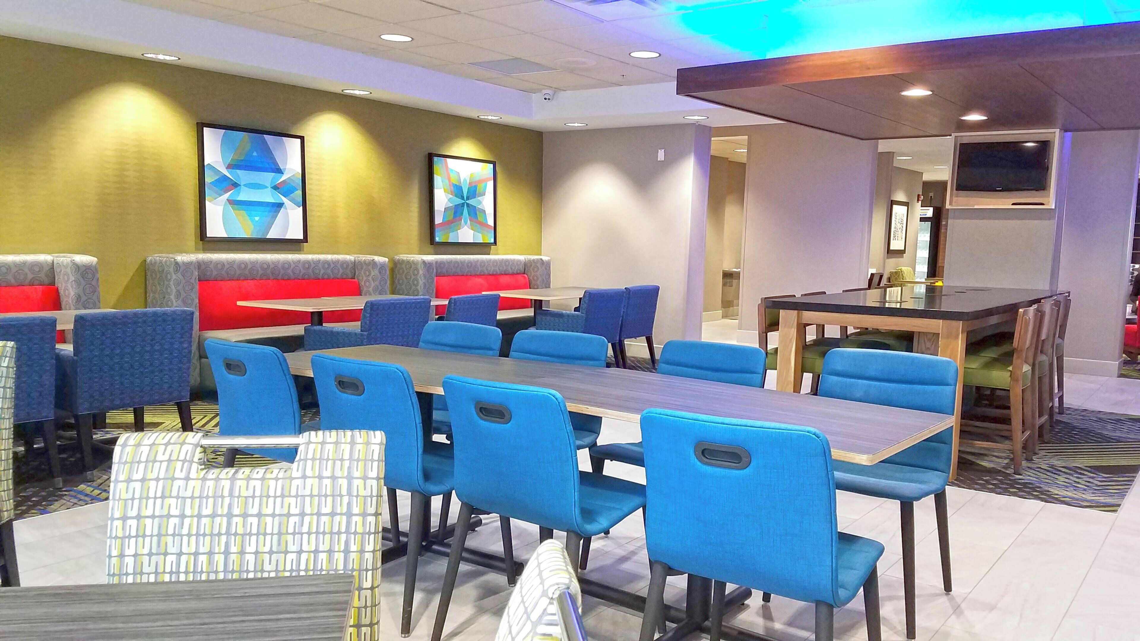 Un comedor de hotel con cabinas y mesas, un televisor de pantalla plana y arte abstracto en las paredes.