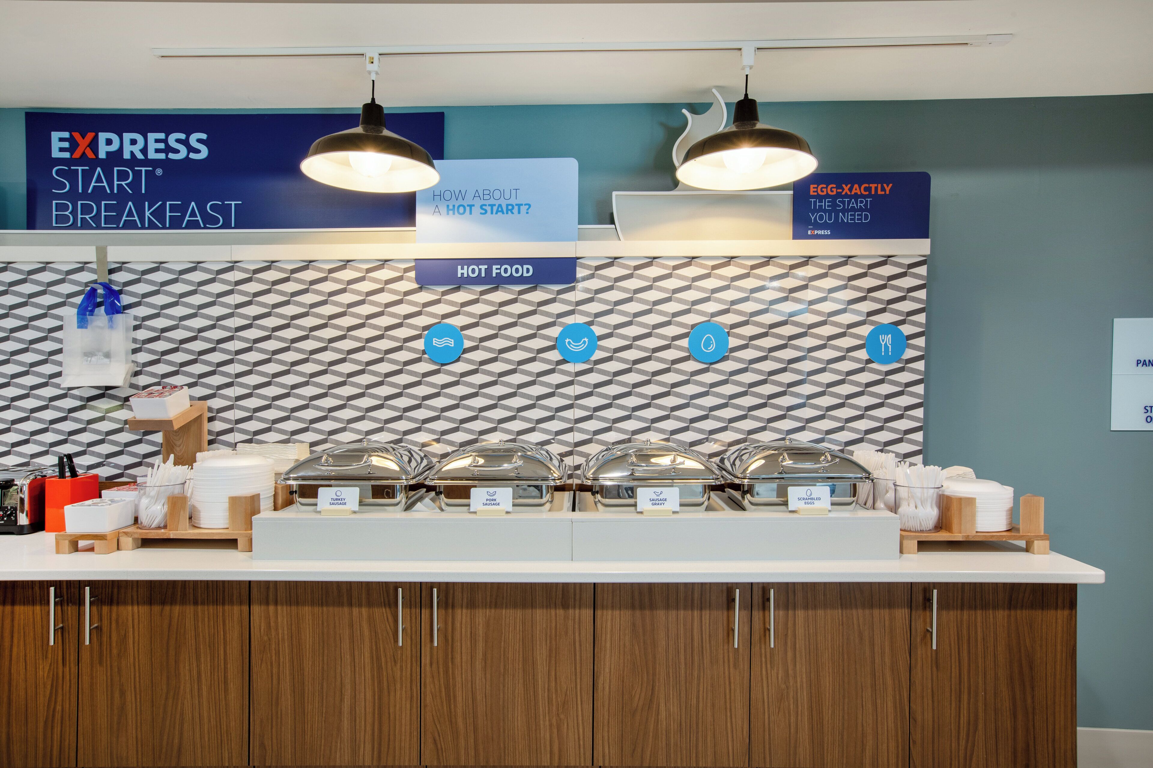A breakfast buffet area with labeled food stations including turkey sausage, pork sausage, sausage gravy, scrambled eggs, and egg-xactly.