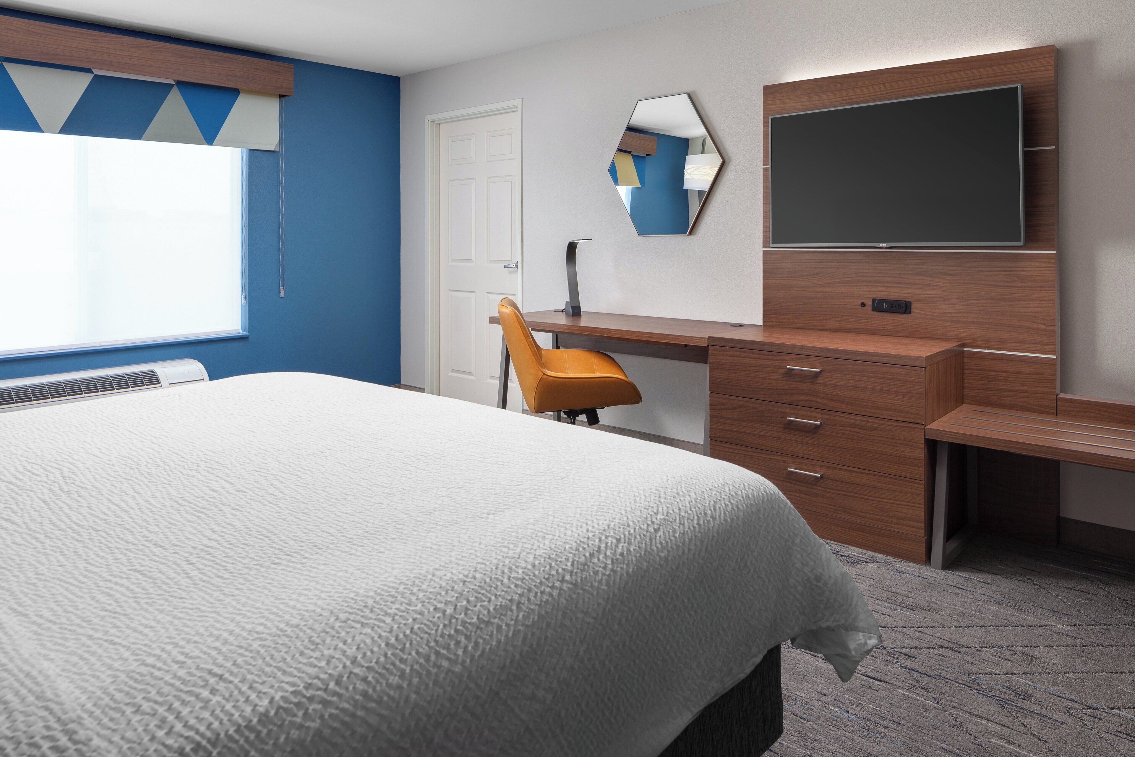 A hotel room with a bed, a desk, a chair, a TV, and a mirror.