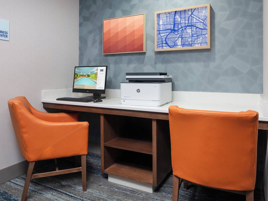Un espacio de trabajo con dos sillas naranjas, un escritorio, una computadora e impresora.