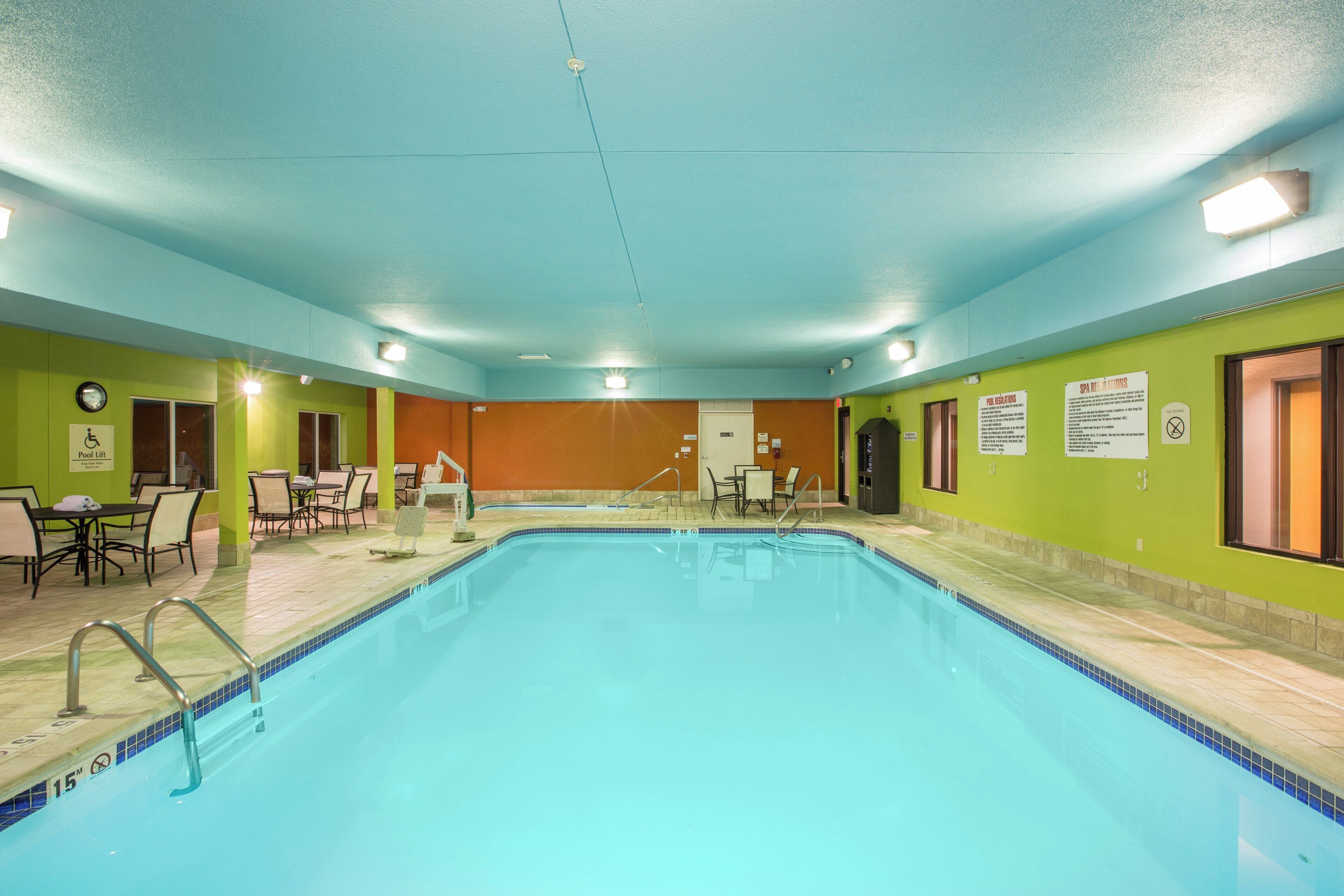 A swimming pool with a lifeguard chair, pool lift, and a poolside seating area with tables and chairs.