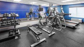 Un gimnasio con equipo de ejercicio, una banca y mancuernas.