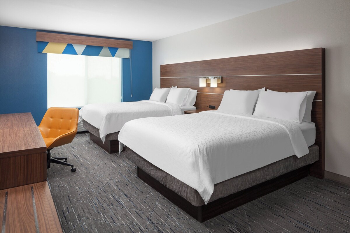 Une chambre d’hôtel avec deux lits, un bureau, une chaise orange et une grande fenêtre.