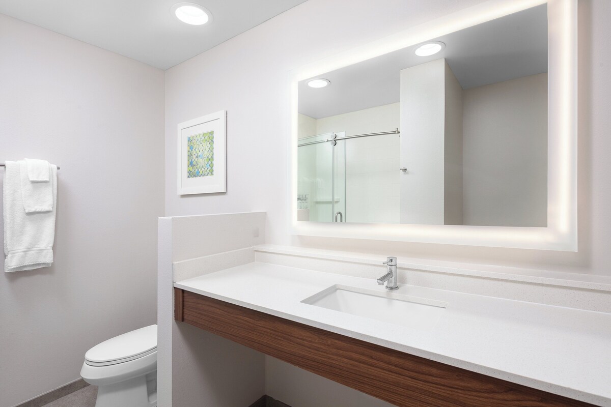 Une salle de bain moderne avec un lavabo blanc, un meuble-lavabo en bois, une cabine de douche en verre et un tableau encadré au mur.