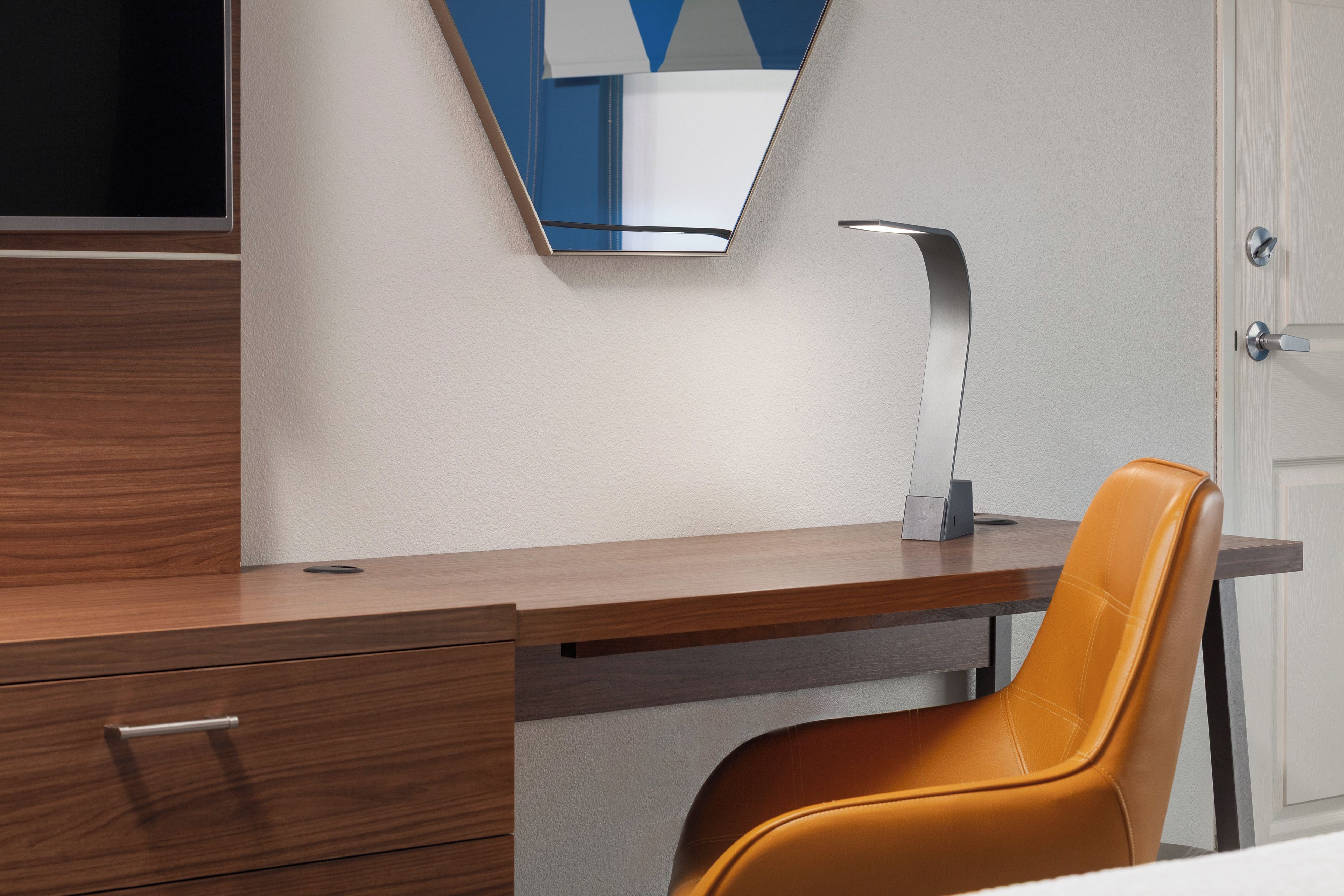 A modern room with a wooden desk, a single chair, a flat-screen TV, and a door.