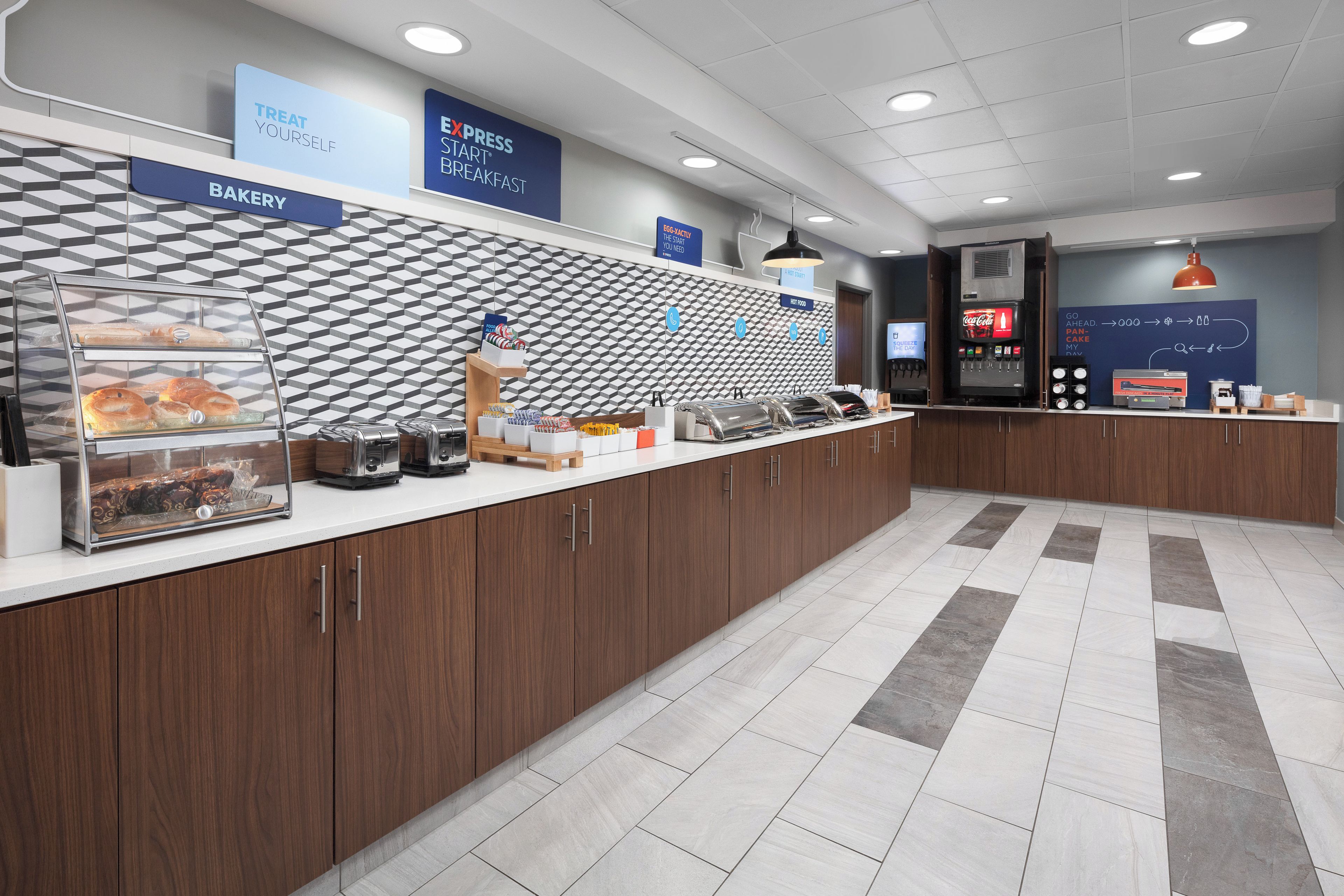 A breakfast area with a bakery display, a Coca-Cola dispenser, and a sign for a hot food station.
