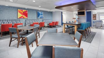 Un comedor de hotel moderno con diversas opciones de asiento, incluidas mesas y cabinas, y una pantalla grande para presentaciones.