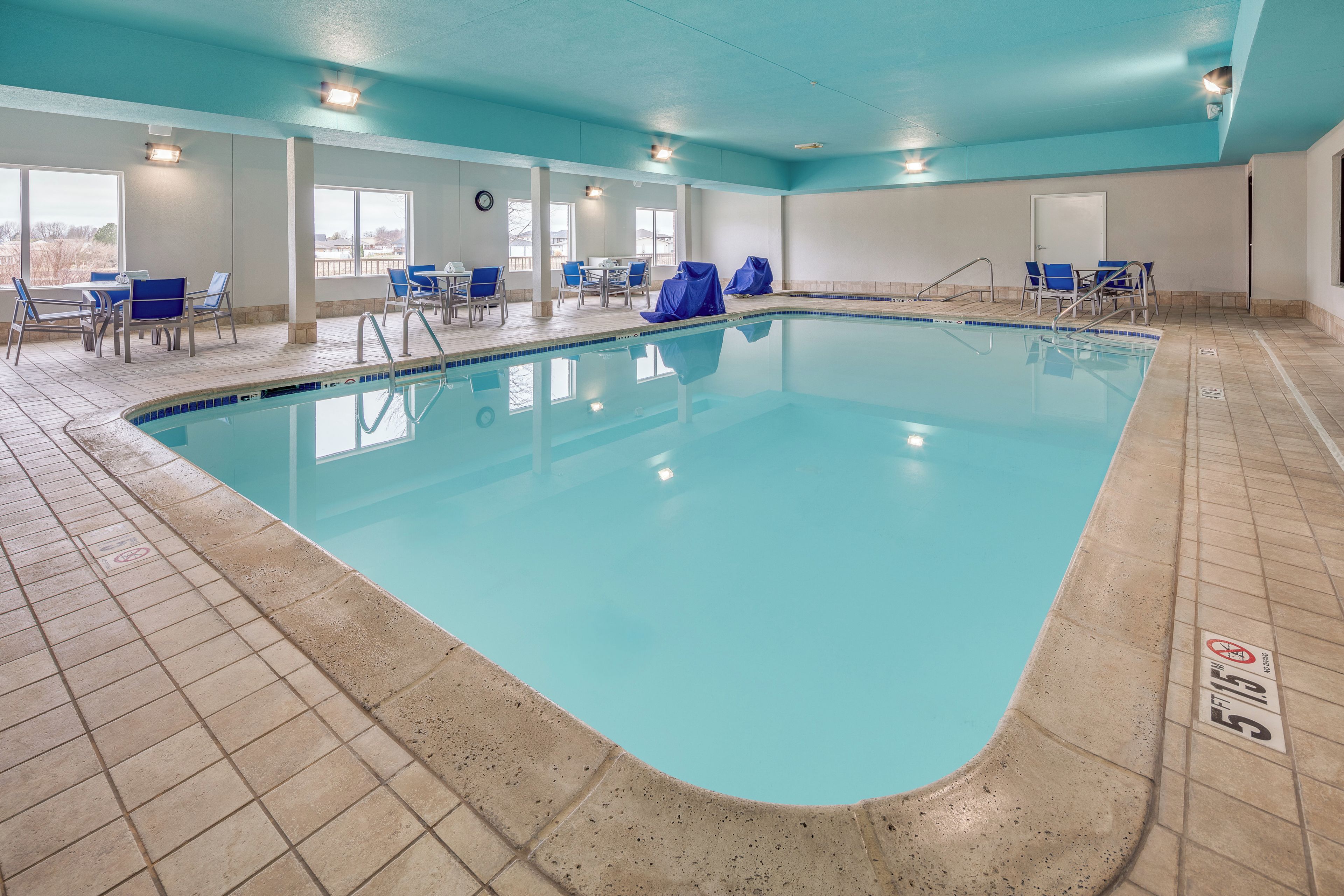 A swimming pool with tiled flooring, covered chairs, and a clock on the wall.