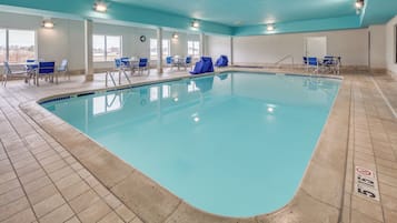 A swimming pool with tiled flooring, covered chairs, and a clock on the wall.