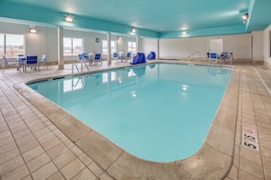Una piscina con suelo de baldosas, sillas cubiertas y un reloj en la pared.