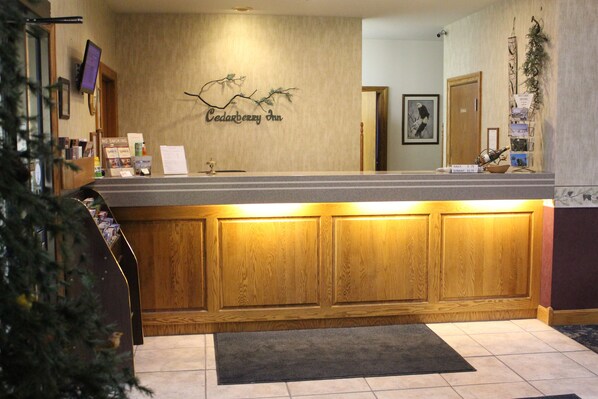 Un mostrador de recepción con diseño de paneles de madera, el letrero de Cedarberry Inn, una planta pequeña y una botella de vino en la barra.