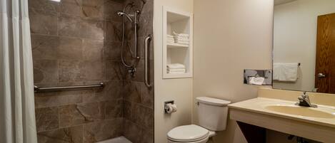 A modern bathroom with a walk-in shower, toilet, sink, and a mirror with lights.