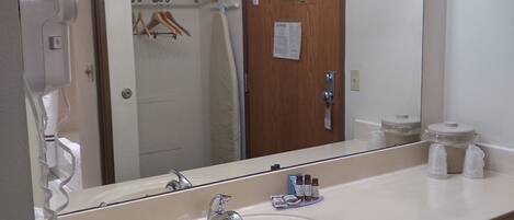 A hotel bathroom with a large mirror, vanity, and a hairdryer.
