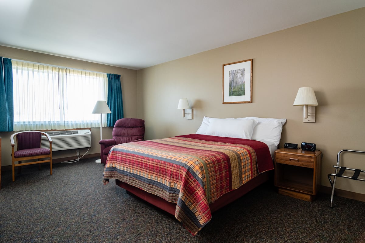 A hotel room with a bed, a chair, a bedside table, a lamp, and a picture on the wall.