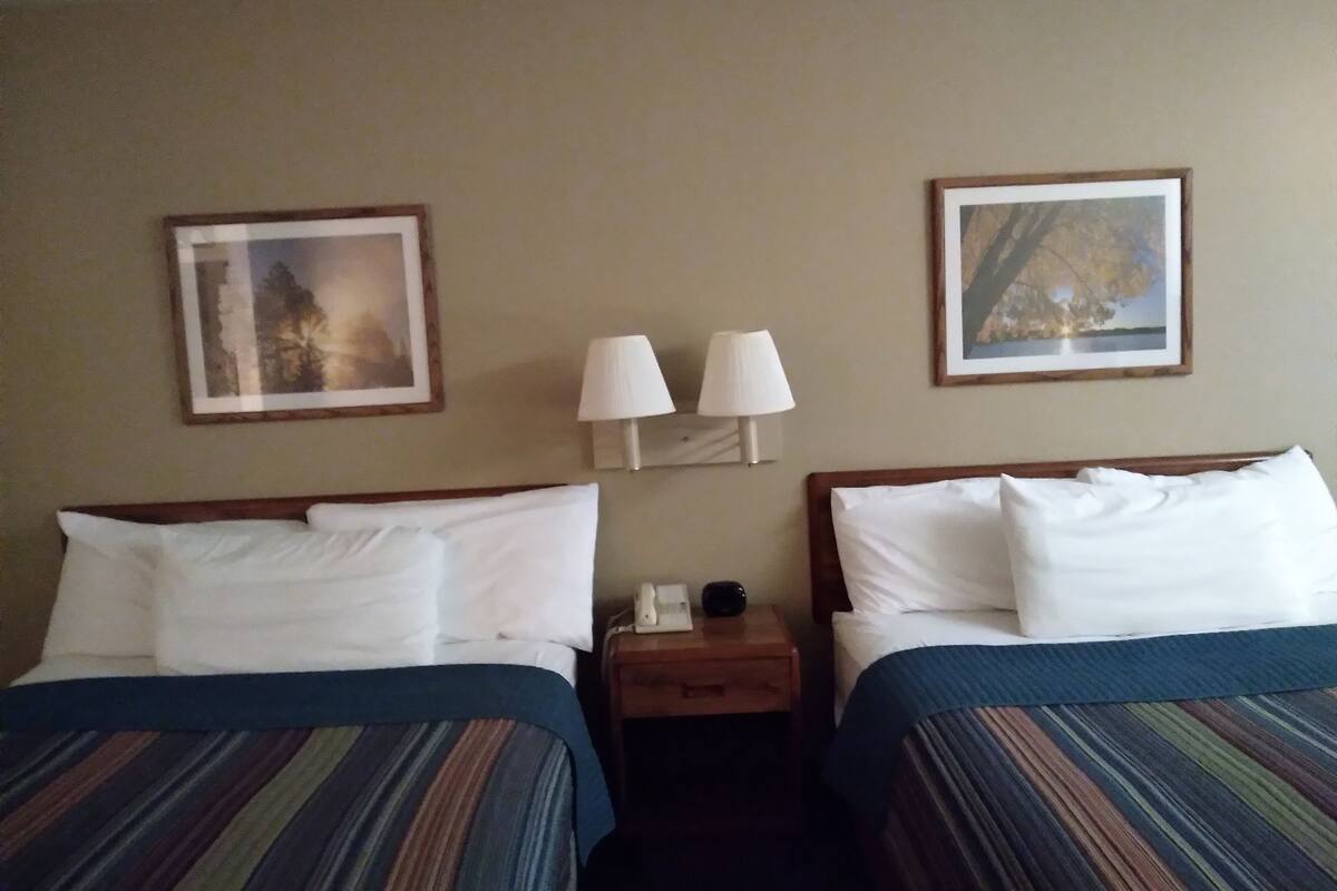 A hotel room with two beds, each with a striped bedspread, two wall-mounted lamps, and framed pictures above the beds.