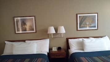 A hotel room with two beds, each with a striped bedspread, two wall-mounted lamps, and framed pictures above the beds.