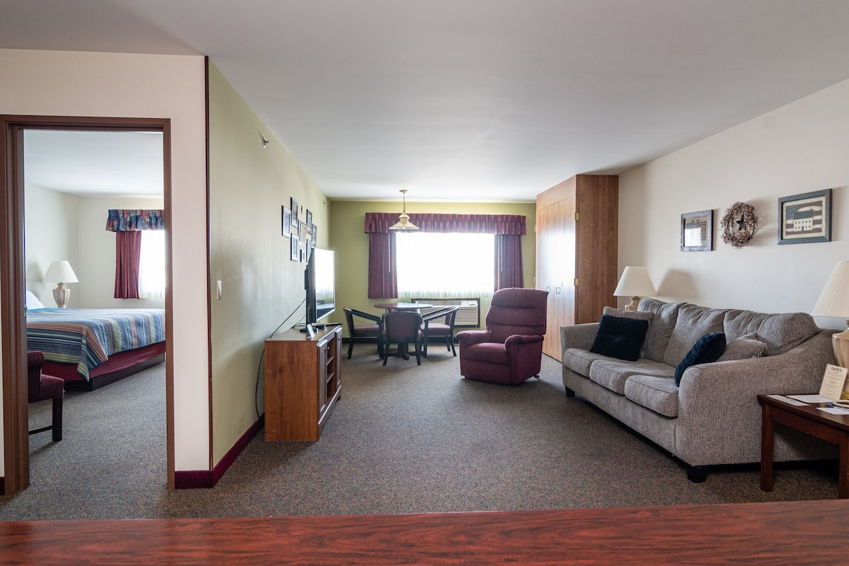 A compact living space with a bed, sofa, armchair, and a small dining table.