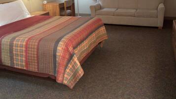 Habitación de hotel con cama, sofá, dos lámparas, ventana con cortinas y suelo alfombrado.