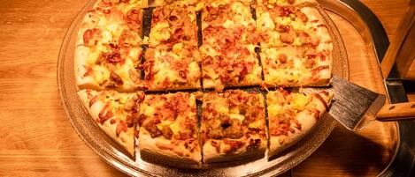 Pizza på et træbord med en pizzaskærer og en bakke.