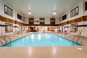 An indoor swimming pool with multiple lanes, lounge chairs, and a bar area.