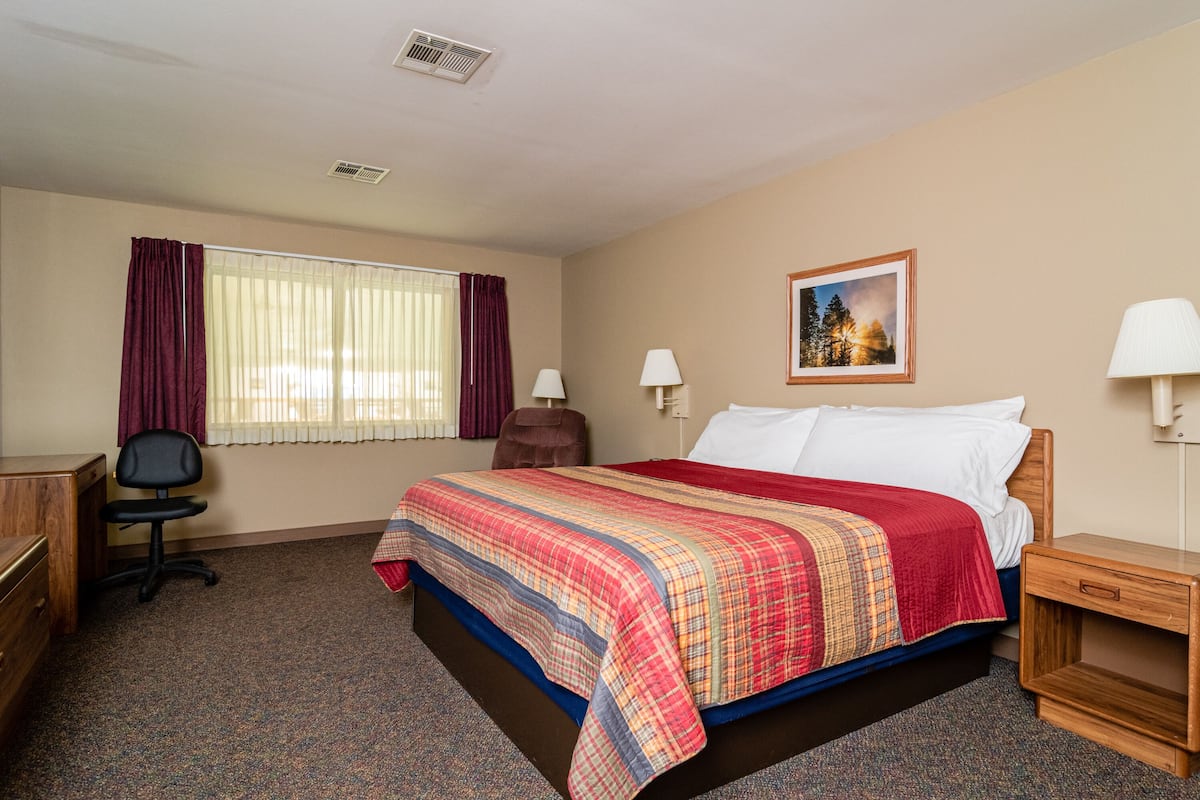 A hotel room with a bed, desk, chair, and a painting on the wall.
