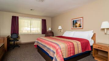 A hotel room with a bed, desk, chair, and a painting on the wall.