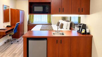 Habitación de hotel compacta con kitchenette, cama con vistas, escritorio con silla y un refrigerador pequeño.