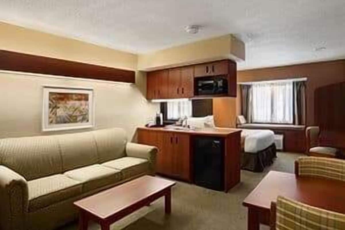 A compact hotel room with a sofa, a small dining table, a kitchenette, and a bed.