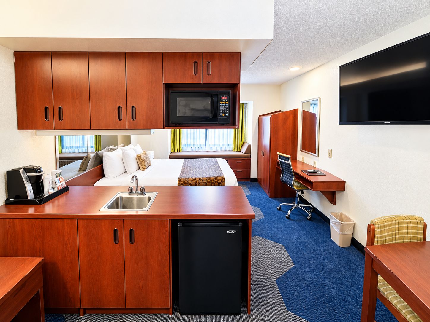 Een compacte hotelkamer met kitchenette, een bed, een bureau en een televisie.