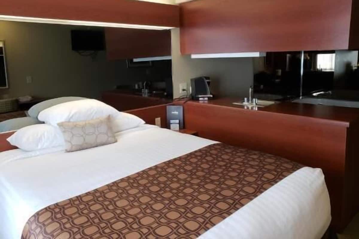A hotel room with a large bed, a desk with a computer, a flat-screen TV, and a minibar.
