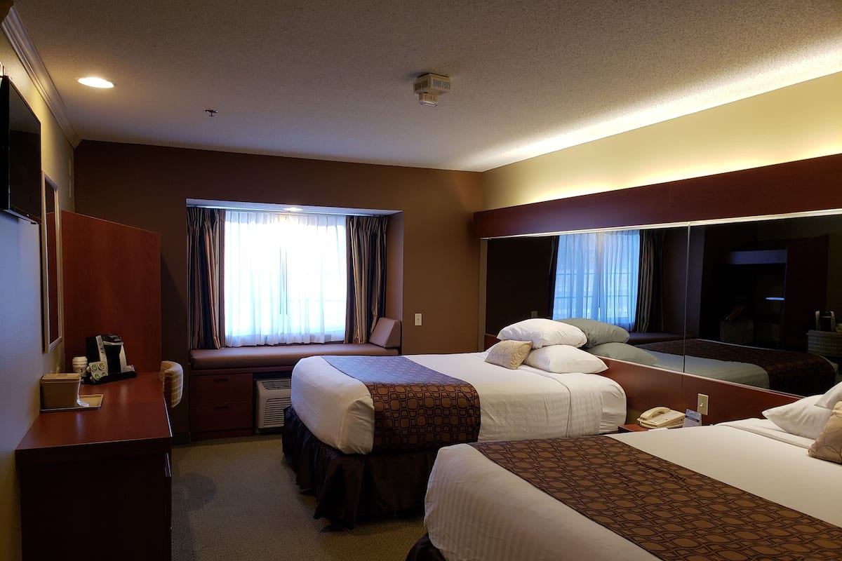 A hotel room with two beds, a desk, a mirror, and a window with curtains.
