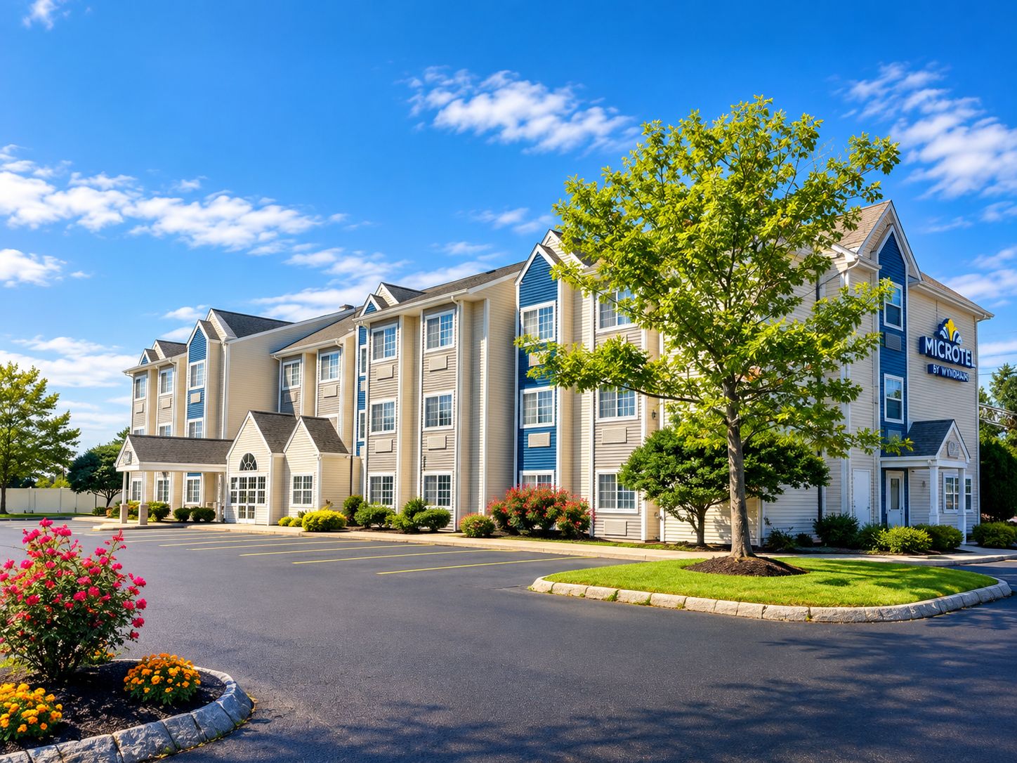 A multi-story hotel with a central courtyard, a parking lot, and a clear sky.