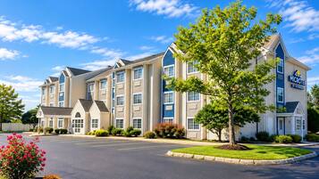 A multi-story hotel with a central courtyard, a parking lot, and a clear sky.