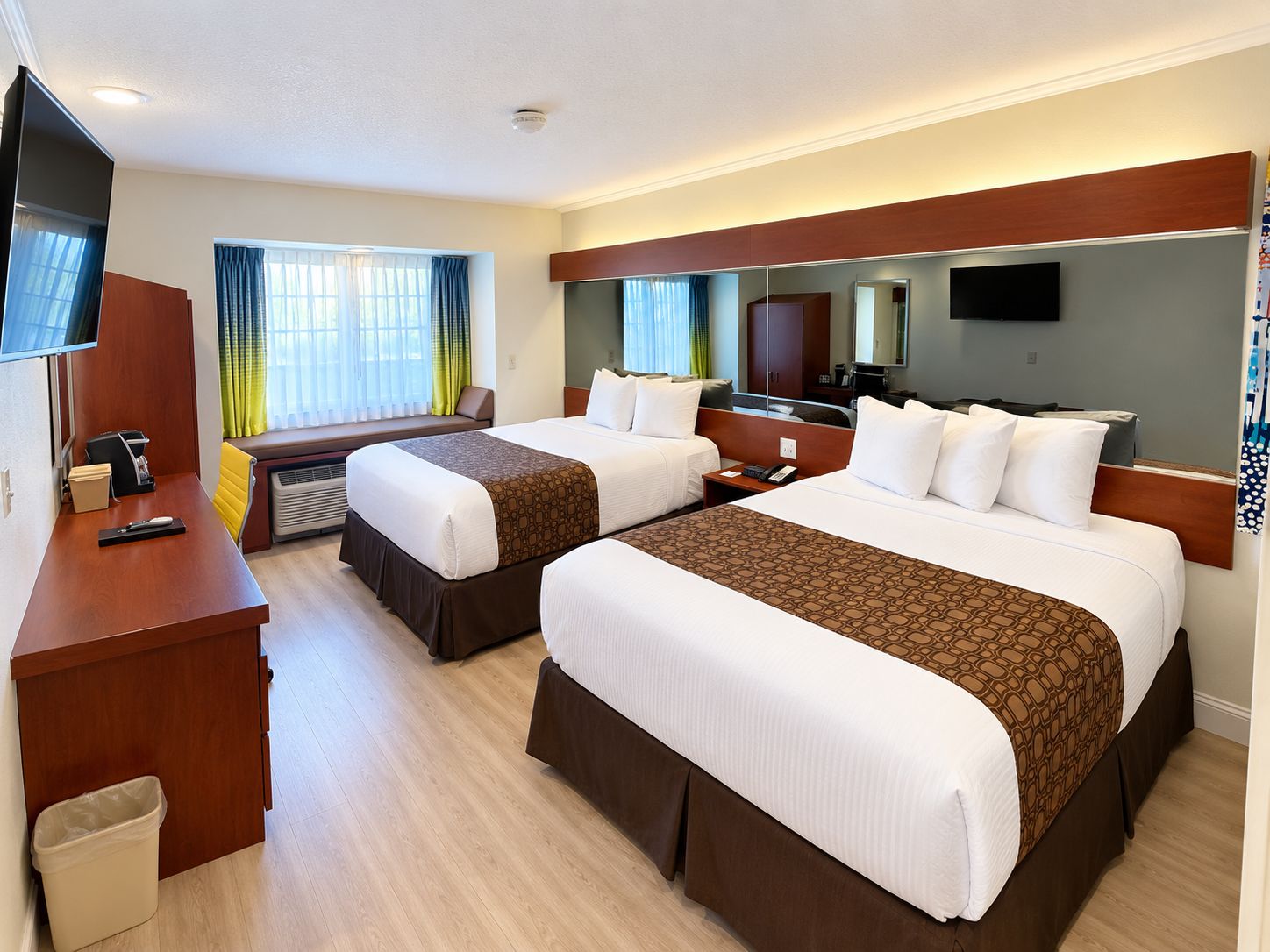 A hotel room with two beds, a desk, a TV, and a window with curtains.