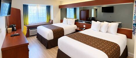 A hotel room with two beds, a desk, a TV, and a window with curtains.