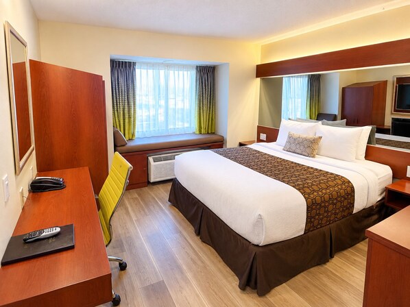 Habitación de hotel con una cama grande, un escritorio con teléfono, una silla, una ventana con cortinas y un televisor.