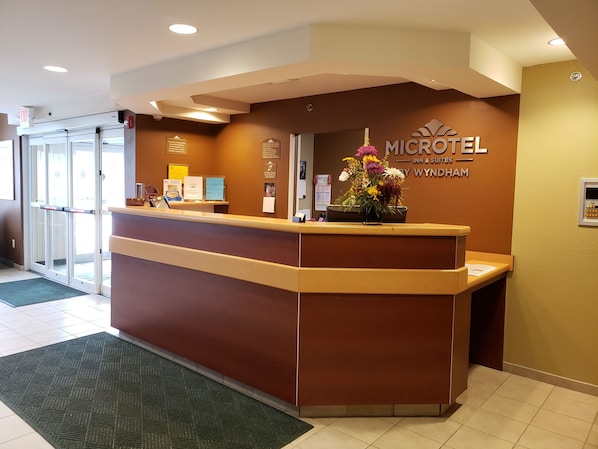 A reception desk at a Microtel Inn & Suites with a brown counter, a flower arrangement, and a sign above the desk. - Microtel Inn & Suites by Wyndham Dover (Dover)