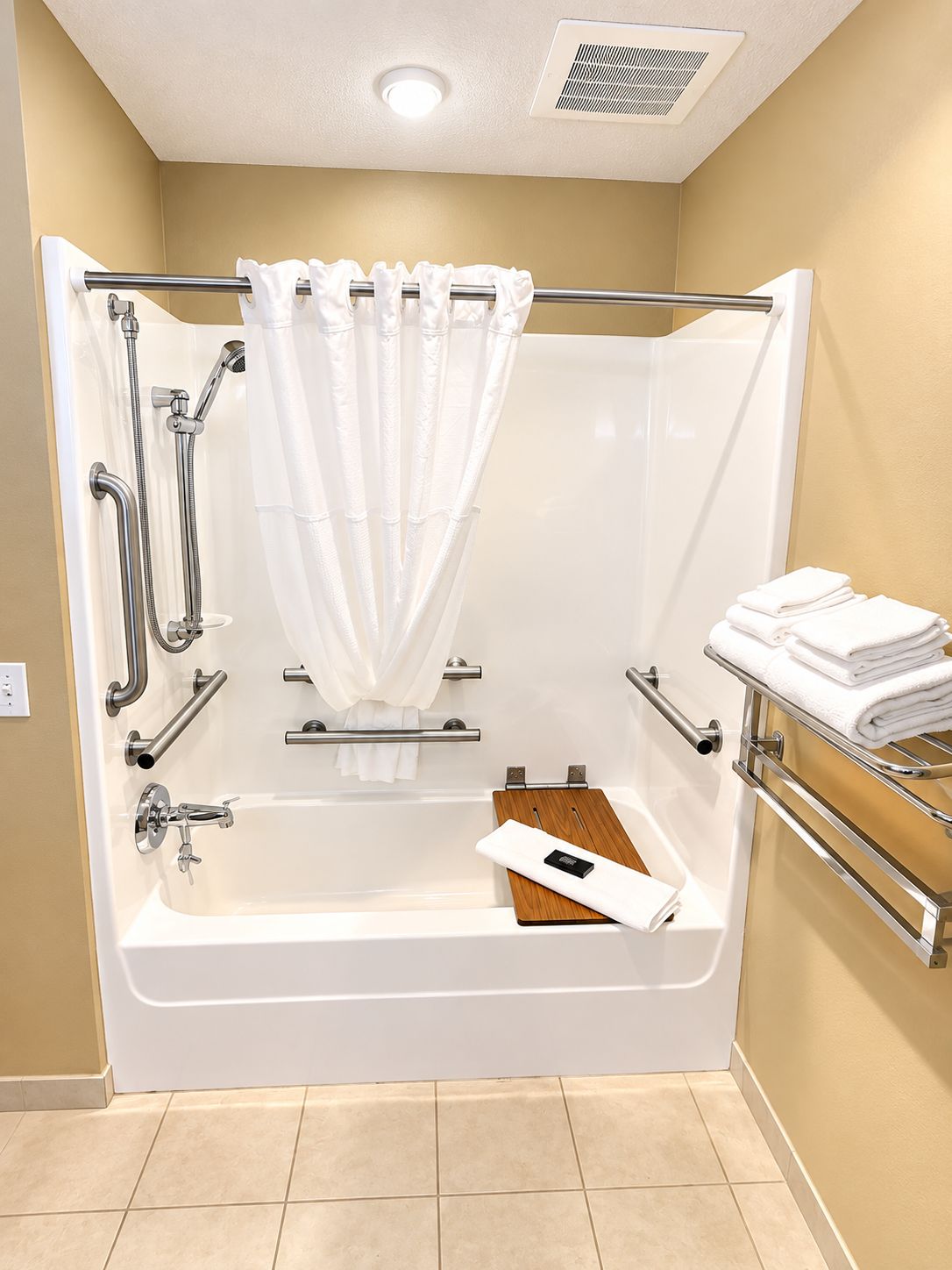 A modern bathroom with a walk-in shower, grab bars, a towel rack, and a wooden bath mat.