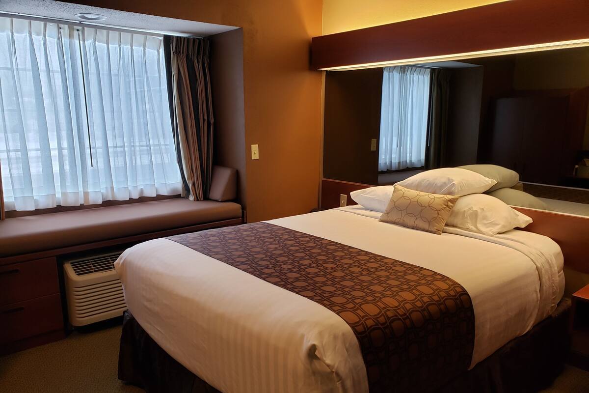 A hotel room with a large bed, a bedside table, a window with curtains, and a wall-mounted TV.