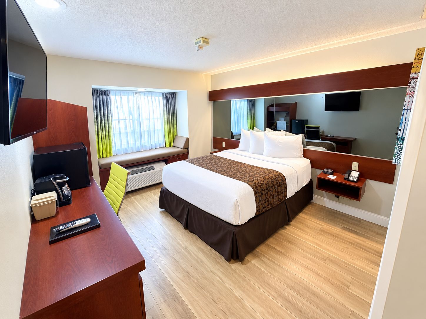 A hotel room with a bed, bedside table, TV, and a window with curtains.