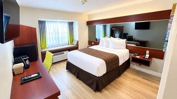 Quarto de hotel com cama, mesa de cabeceira, televisão e janela com cortinas.