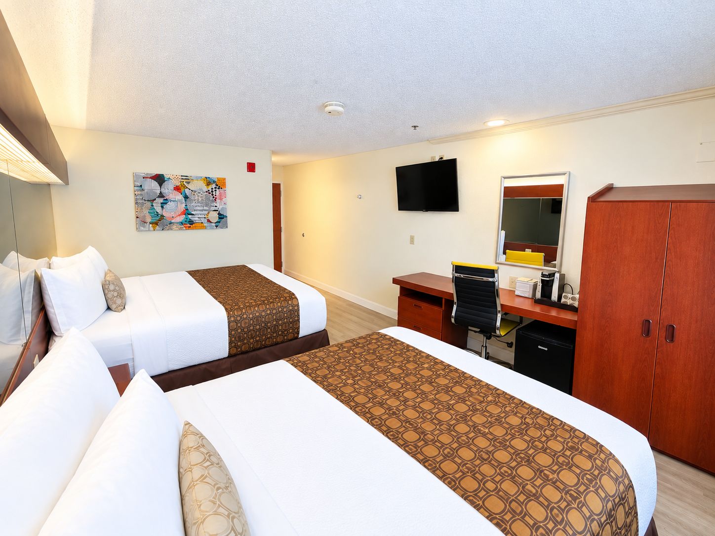 Ett hotellrum med två sängar, ett skrivbord, en stol, en tv och en garderob.